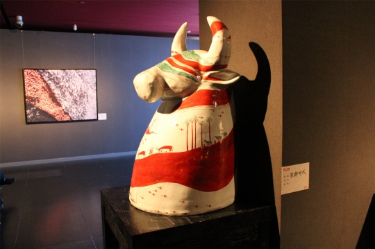 本次展出的作品超出了寻常意义上的陶瓷艺术品,涵盖雕塑、壁画、装置等类型,作品东方韵味十足,风格清新、极简,以莲为题创作的一组栖于墙面的金色作品是禅意浓浓,另有白色瓷板上温婉的睡莲,有以牛为思维的落脚点的憨态可掬的雕塑,有在草原休憩的古风古韵的马等等。在现场,十位身着彩衣的高挑女子穿行于作品间,堪称一道美丽的风景,服饰飘逸,图案与作品中的元素并无二致,经介绍才得知,这是以朱乐耕作品《五彩云》为蓝本设计的服装,一位古典女子在彩云间的弹奏更是如歌如诉,这些艺术衍生品、流动于展厅的艺术品给人眼前一亮之感,对展览