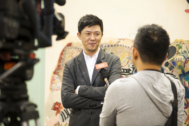 董梦阳在诚品画廊展位接受采访，这里有一张艺术家王玉平创作的《董梦阳》
