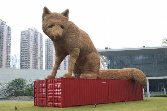 来自英国艺术家艾利克斯·林斯勒的作品，近7米高的《城市狐狸》，以稻草包裹住的肤质，略带忧伤的神情注视着芸芸众生——它千里迢迢远涉而来，试图寻找一处生命的乐园。借由它的存在时刻提醒着人们，谋求人与动物之间的和谐共处。（擅长为节日制作大型雕塑与装置的艾里克斯，目前是一名定居在英国曼切斯特的公共艺术家和节目制作人。）
