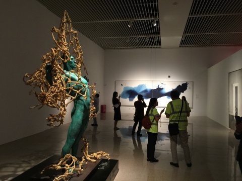 展览现场，左为雕塑家任哲作品《守护者》，远处作品为策展人黄笃为完整本次展览形式，特意加入本次展览的艺术家毛栗子的抽象风格作品
