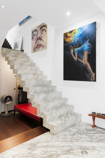 连接一楼和二楼的是一整块大理石做成的悬浮状楼梯，墙上是喻红2014年的作品《天体》（右）和曾梵志的自画像（左）。
